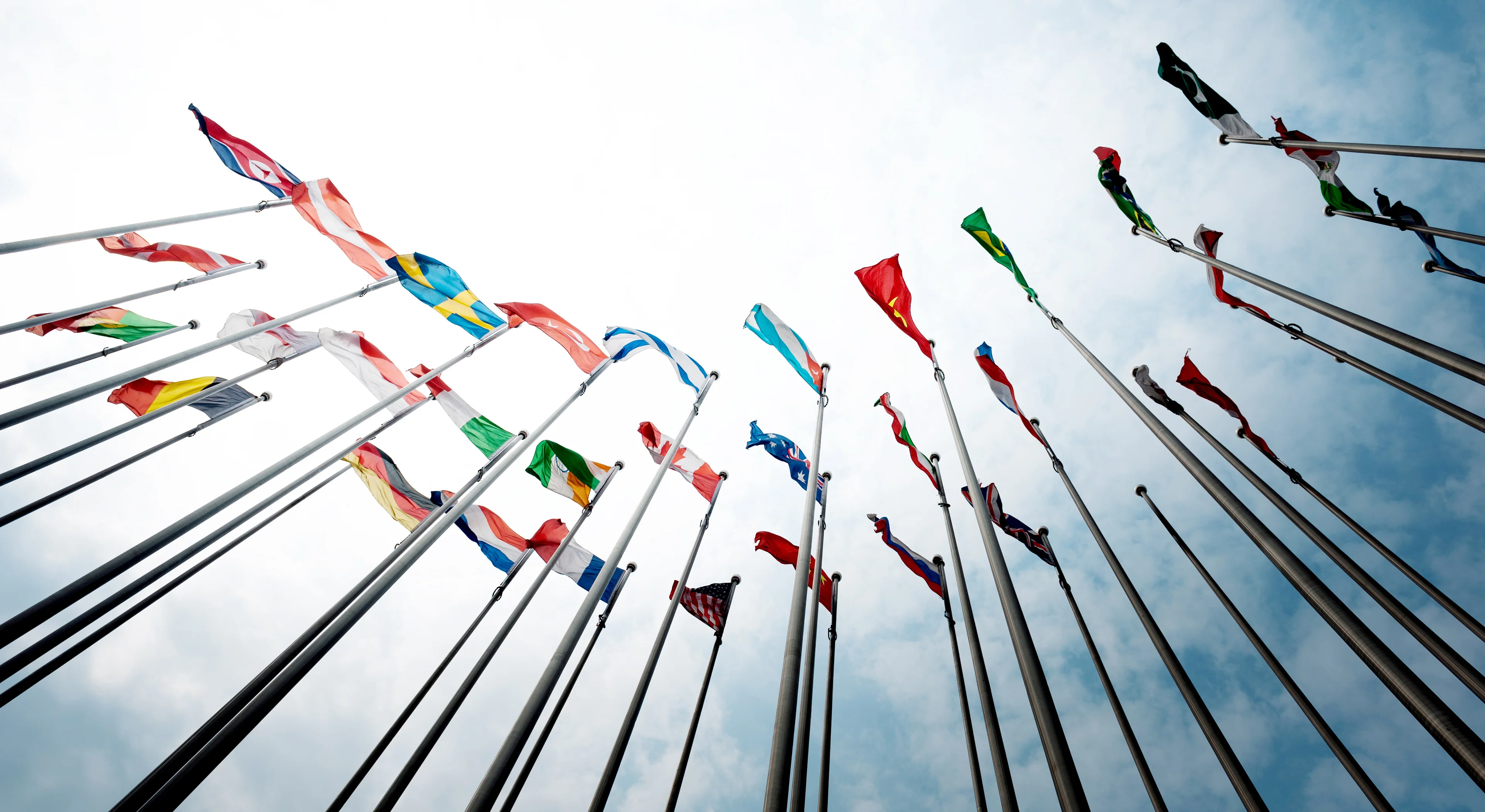 Flags from different countries on poles blowing through the wind.