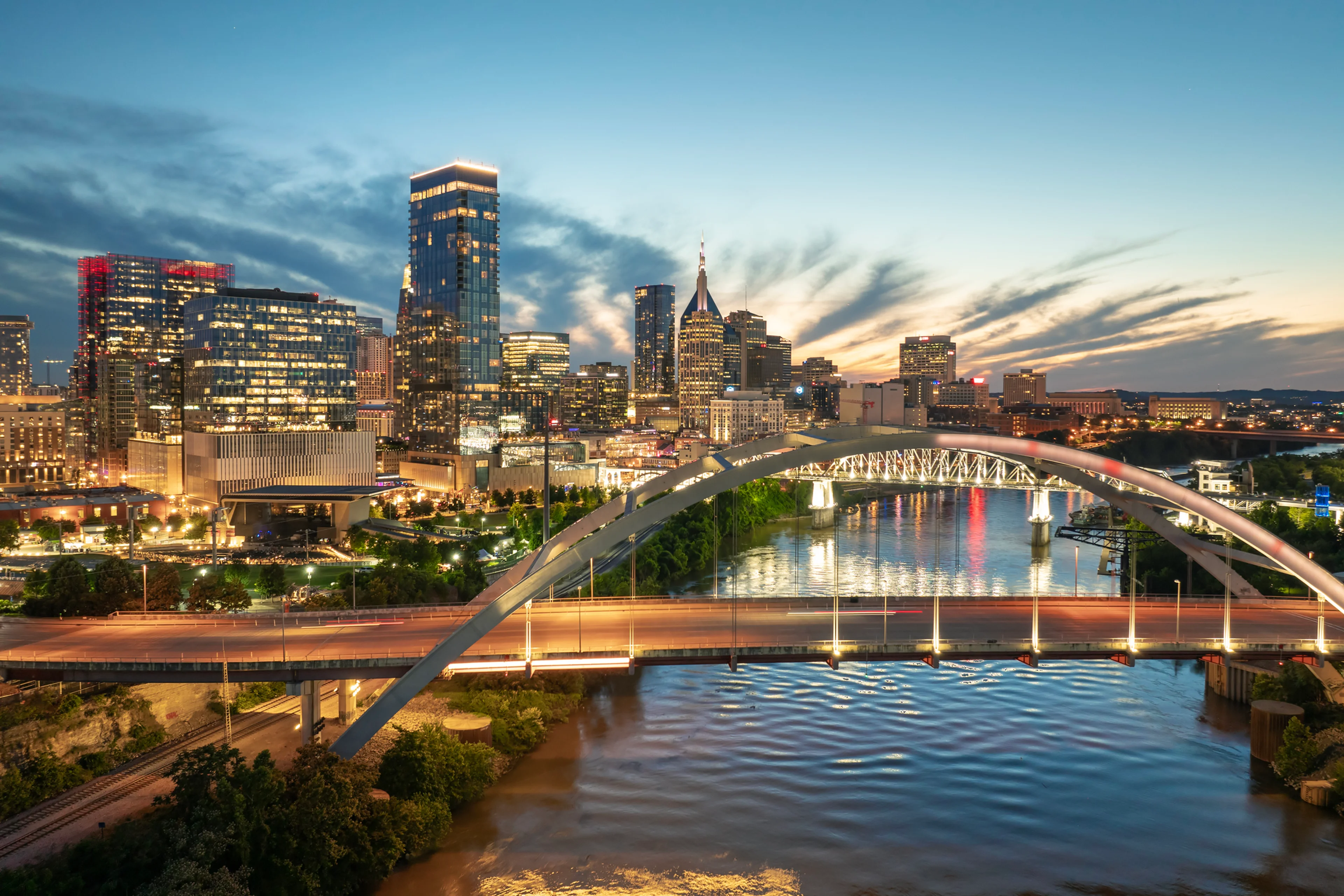 Downtown district of Nashville city in Tennessee, USA at sunset. Cars drive on Korean Veterans Memorial Bridge over Cumberland river. American travel destination